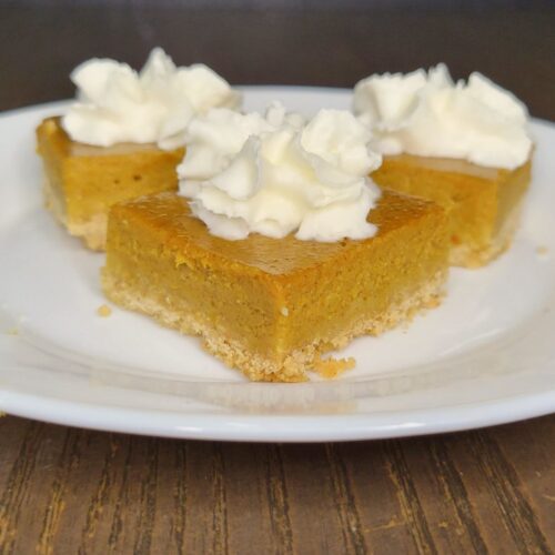 three pumpkin pie bars made with fresh milled flour, topped with a bit of whipped cream and sitting on a white plate.