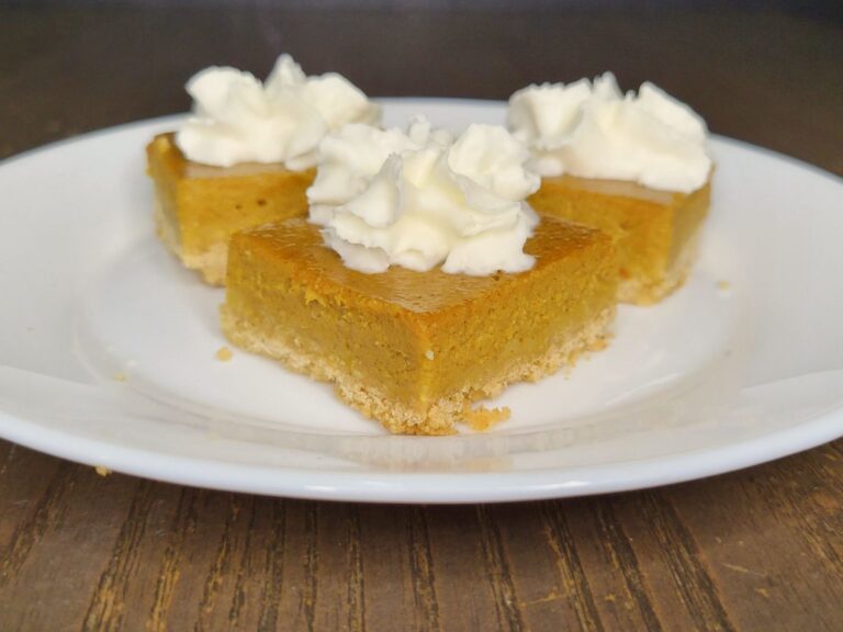 three pumpkin pie bars made with fresh milled flour, topped with a bit of whipped cream and sitting on a white plate.