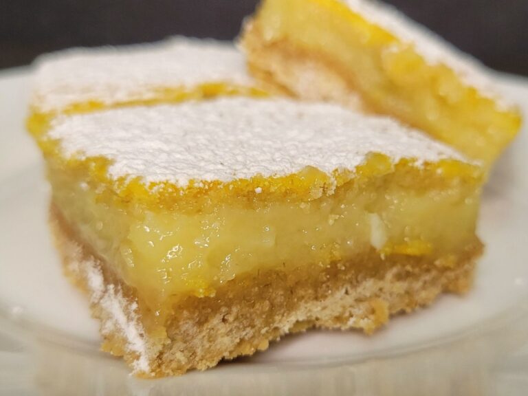 a sliced lemon bar made from fresh milled flour on a plate in front of 2 other lemon squares. All dusted with powdered sugar