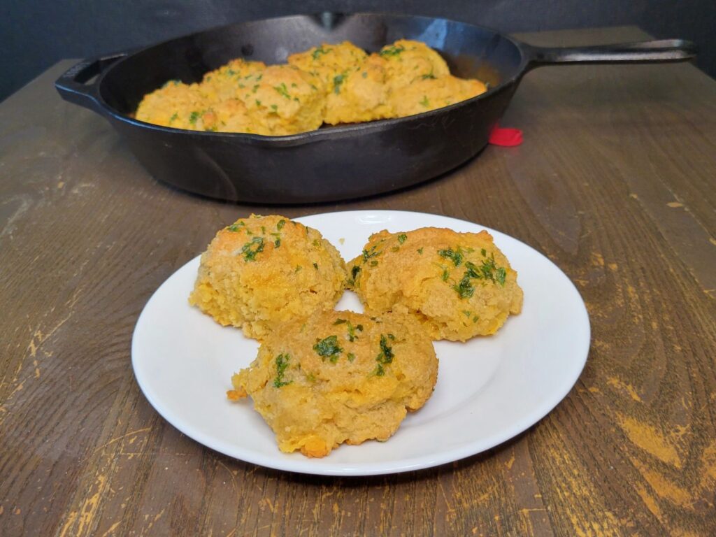 easy garlic cheddar biscuits made with fresh milled flour 3 on a plate, and the rest in the cast iron skillet in the background