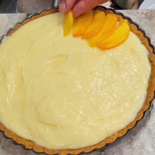 hands putting fresh peaches on a homemade tart filled with pastry cream made from fresh milled flour