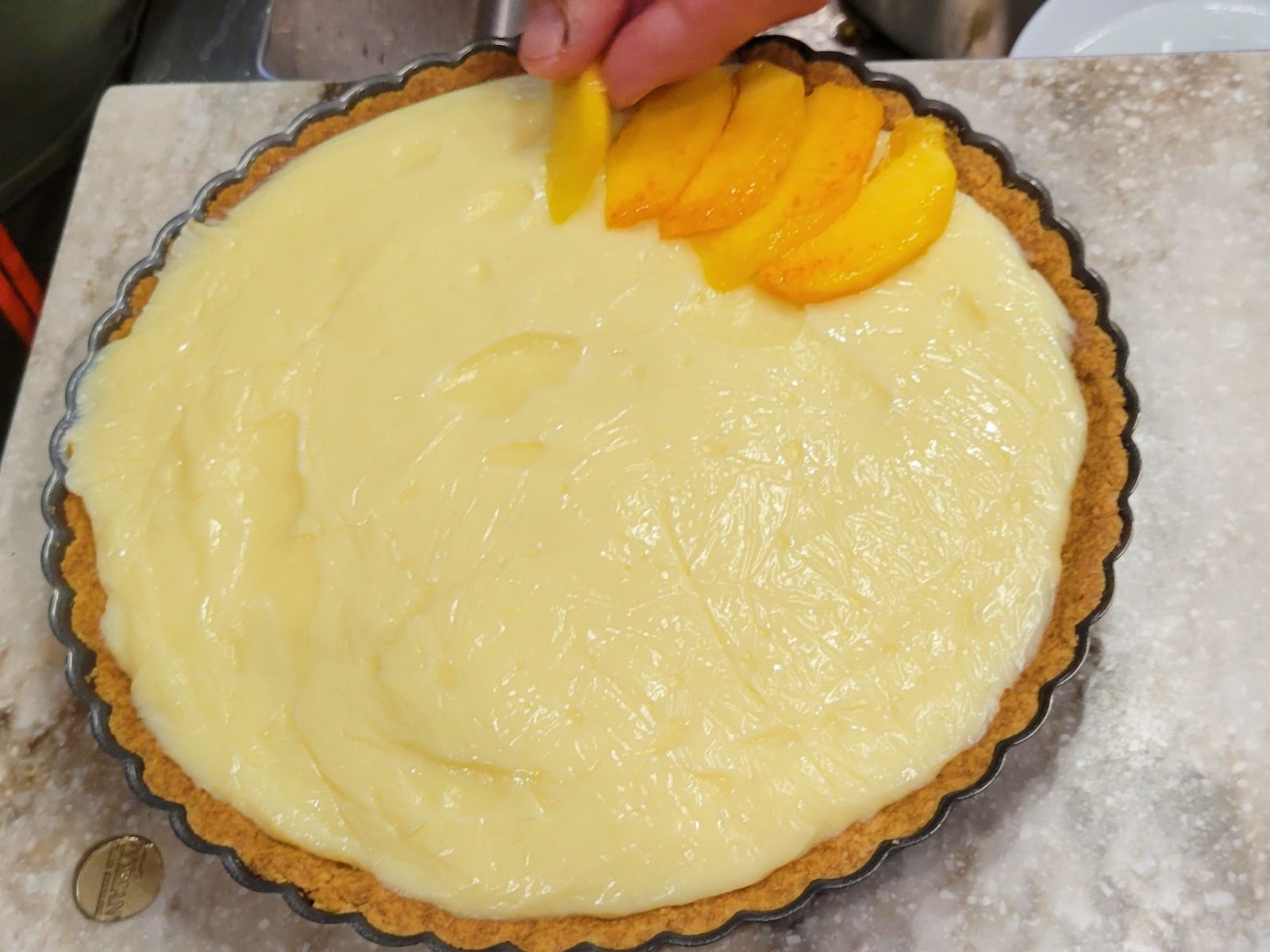 hands putting fresh peaches on a homemade tart filled with pastry cream made from fresh milled flour