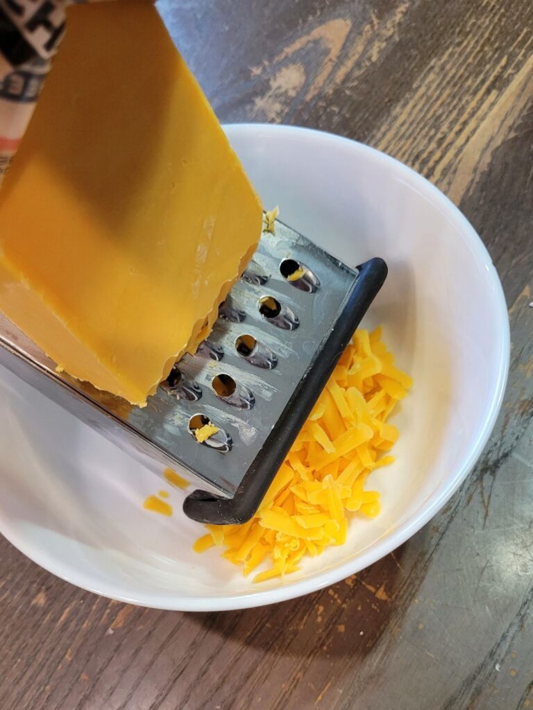 hand shredding cheese with a grater into a bowl