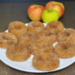 a plate of Apple Cider donuts made with fresh milled flour in front of one green whole apple and two red and yellow whole apples.
