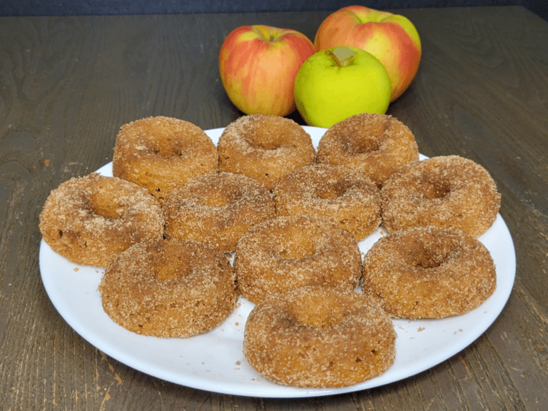 a plate of Apple Cider donuts made with fresh milled flour in front of one green whole apple and two red and yellow whole apples.