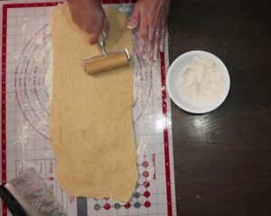 hand using wooden rolling pin to roll dough into a 6 by 20 inch rectangle