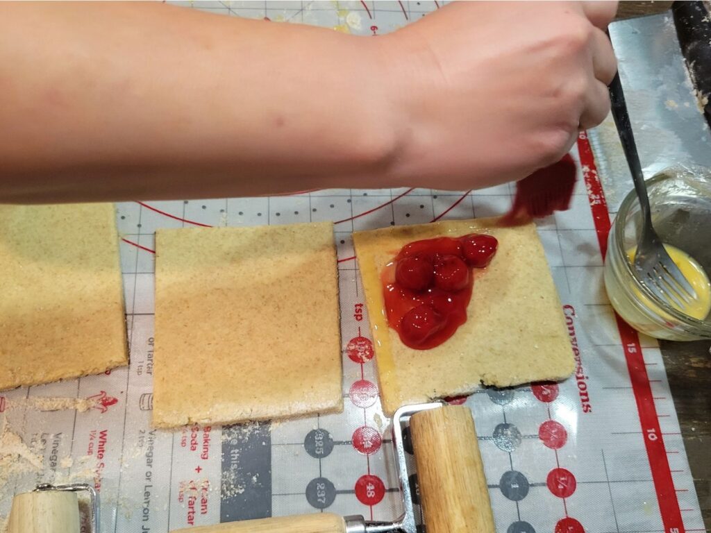 hand placing cherry pie filling into puff pastry made from fresh milled flour