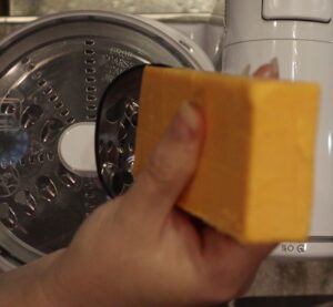 a hand grating a block of cheddar cheese