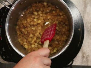 hand making apple spice filling with a spatula in a pot.