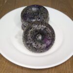 a stack of homemade fresh milled flour blueberry cake donuts on a white plate with one donut facing forward.