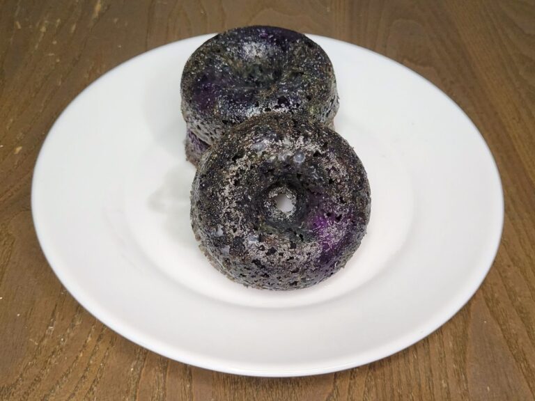 a stack of homemade fresh milled flour blueberry cake donuts on a white plate with one donut facing forward.
