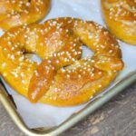 a close up of a salted fresh milled flour soft pretzel on a baking sheet with other soft pretzels