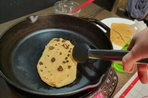 cooking Flatbread made with fresh milled flour on a cast iron skillet with tongs