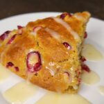 Fresh milled flour cranberry orange scone on a plate drizzled with orange glaze