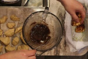 hands using a spoon to dipping the monkey bread pieces into the cinnamon sugar mixture