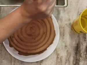 hands piping the top of the fresh milled flour yellow birthday cake with the chocolate ganache buttercream