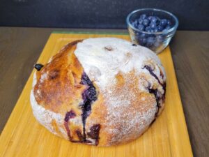 Blueberry Sourdough Bread Boule loaf in front of a bowl of fresh blueberries