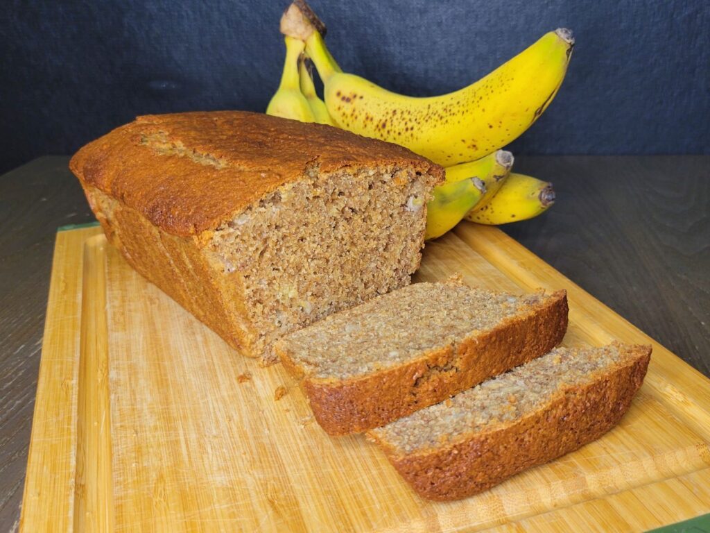 a loaf of fresh milled flour banana bread in front of a bunch of fresh yellow bananas