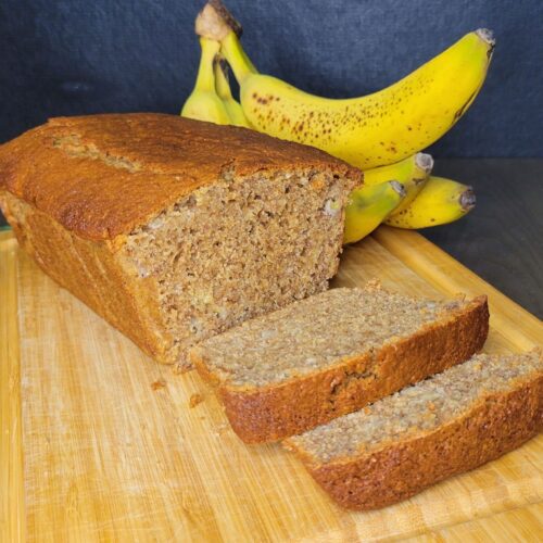 a loaf of fresh milled flour banana bread in front of a bunch of fresh yellow bananas