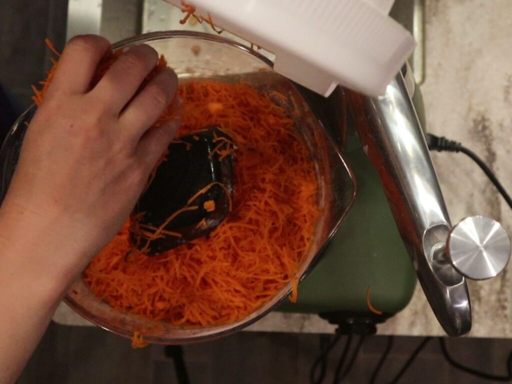 hand adding shredded carrots to the fresh milled flour carrot cake batter in a mixer