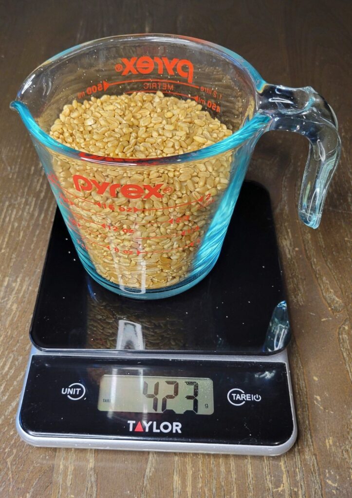 weighing the wheat berries will give you the same weight of flour. Going by weight will give you more accurate results.