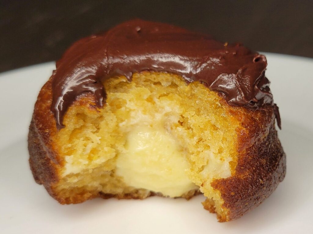 Boston Cream donuts made with fresh milled flour with a bite out of it showing the filling and layers
