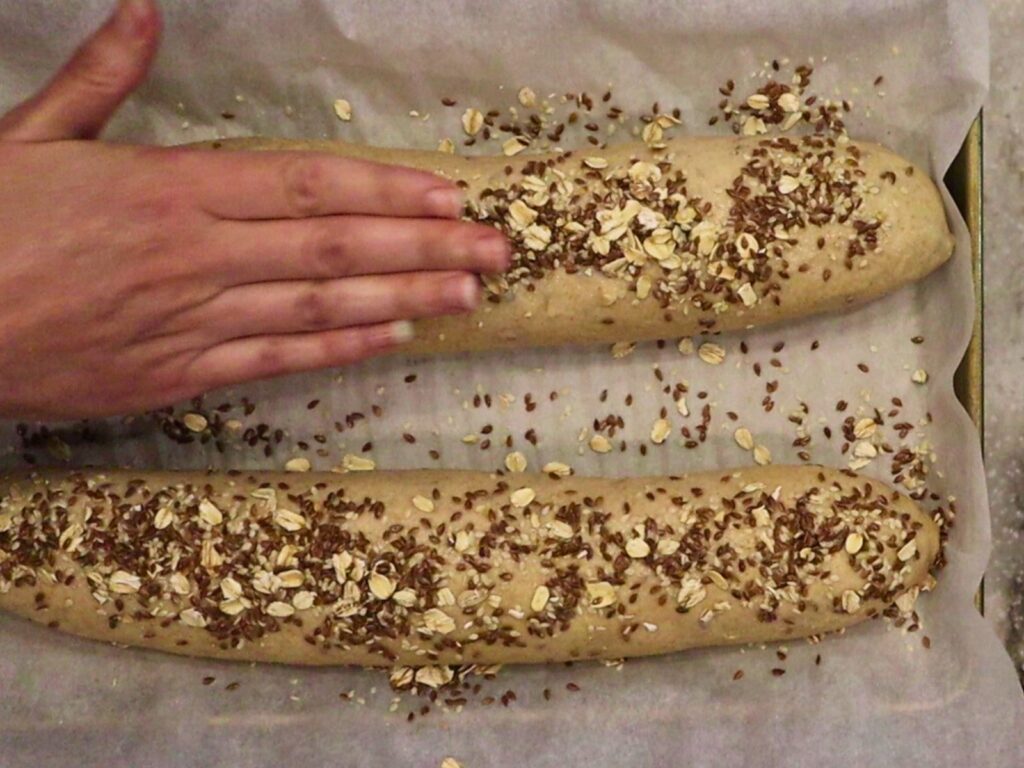 hands pressing the seeds on top of the fresh milled flour seeded honey wheat bread