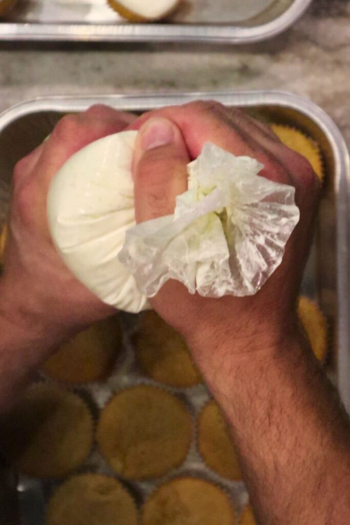 hands using a disposable piping bag to pipe the vanilla bean buttercream on the fresh milled flour cupcakes