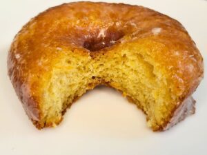 a single yeast glazed donut made with fresh milled flour with a bit out of it showing the inside texture
