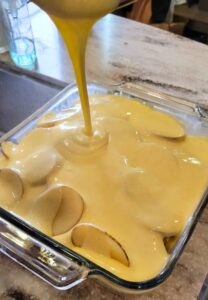 pouring the cheese sauce over the sliced potatoes