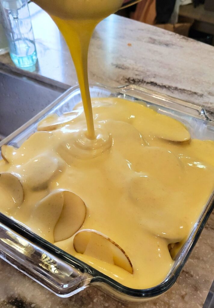 pouring the cheese sauce over the sliced potatoes