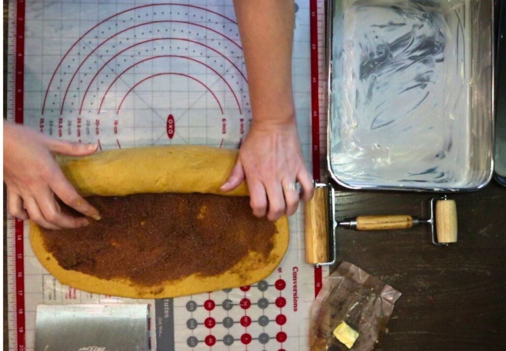 rolling up the pumpkin cinnamon roll dough after filling